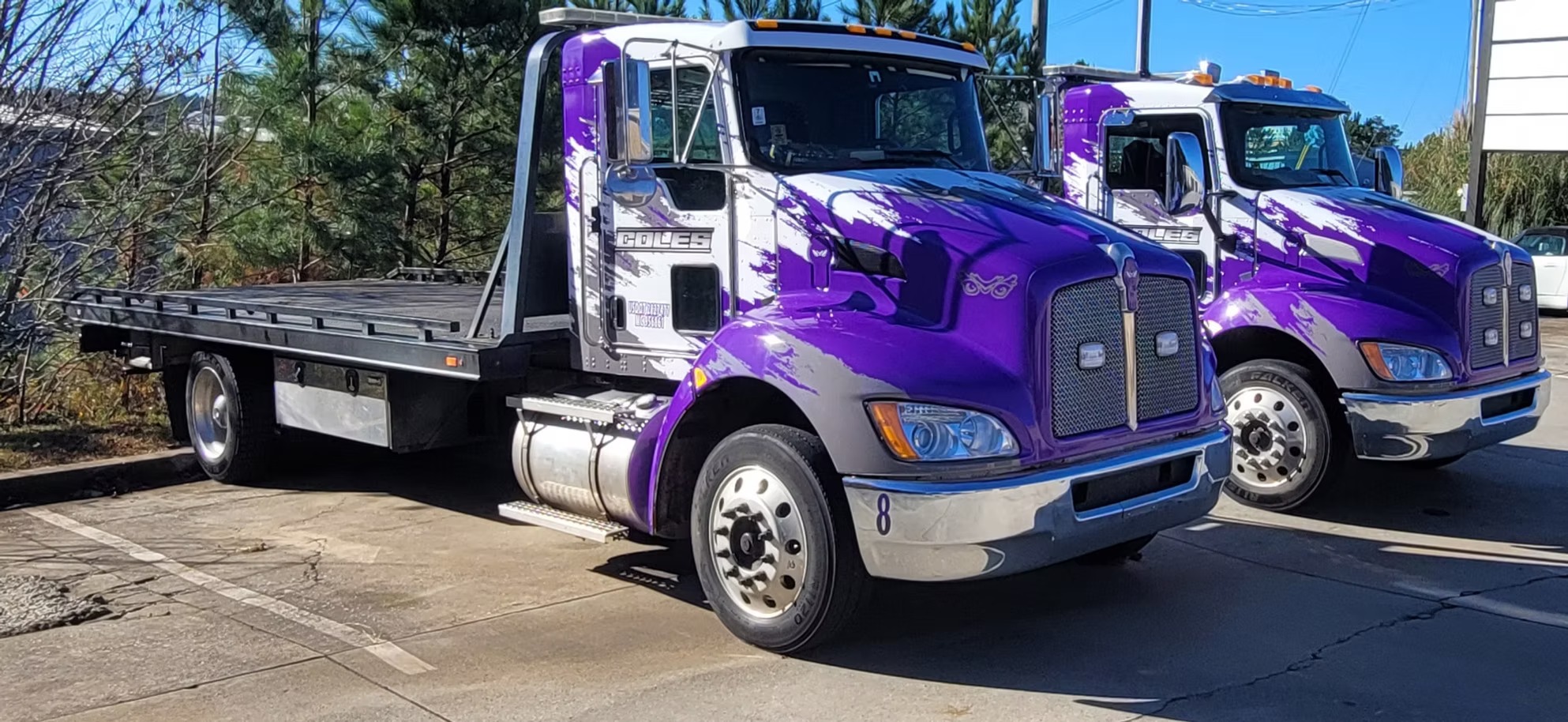 Two flatbed tow trucks with matching purple and white graphics