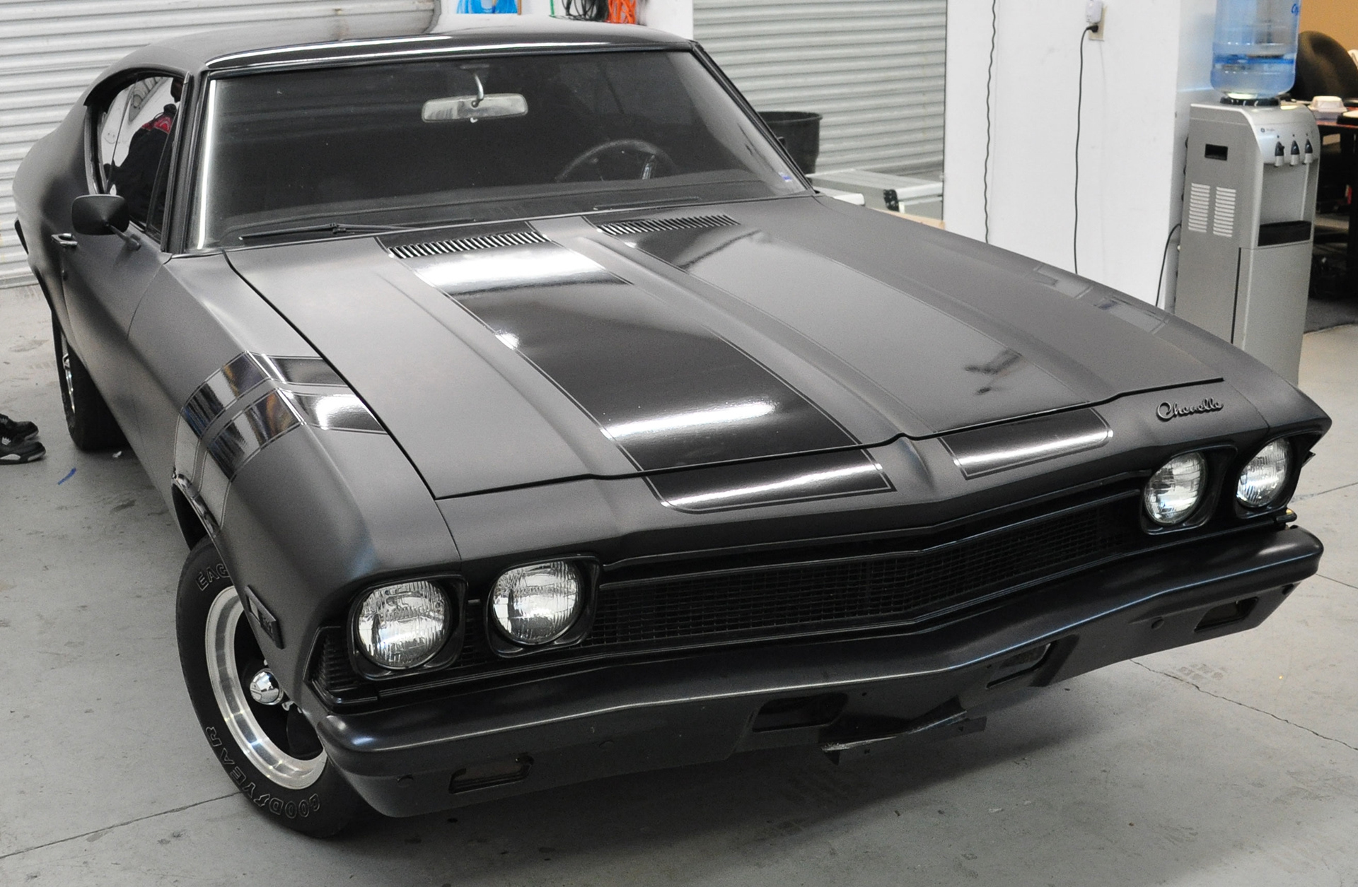 Classic Chevrolet Chevelle with a matte dark finish and glossy black racing stripes in the workshop.