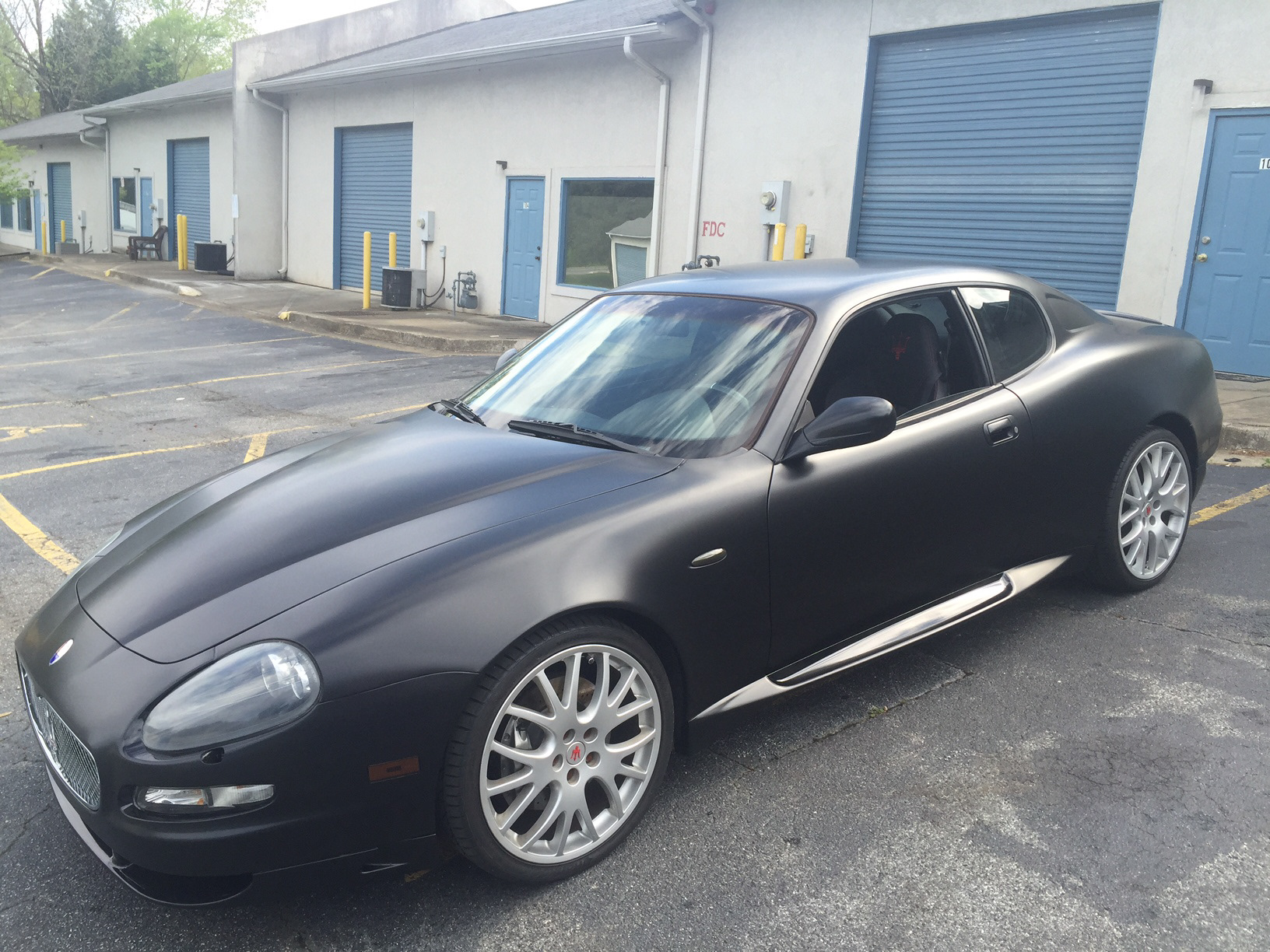 Maserati coupe in satin black with gloss black accents and silver wheels outside the workshop.