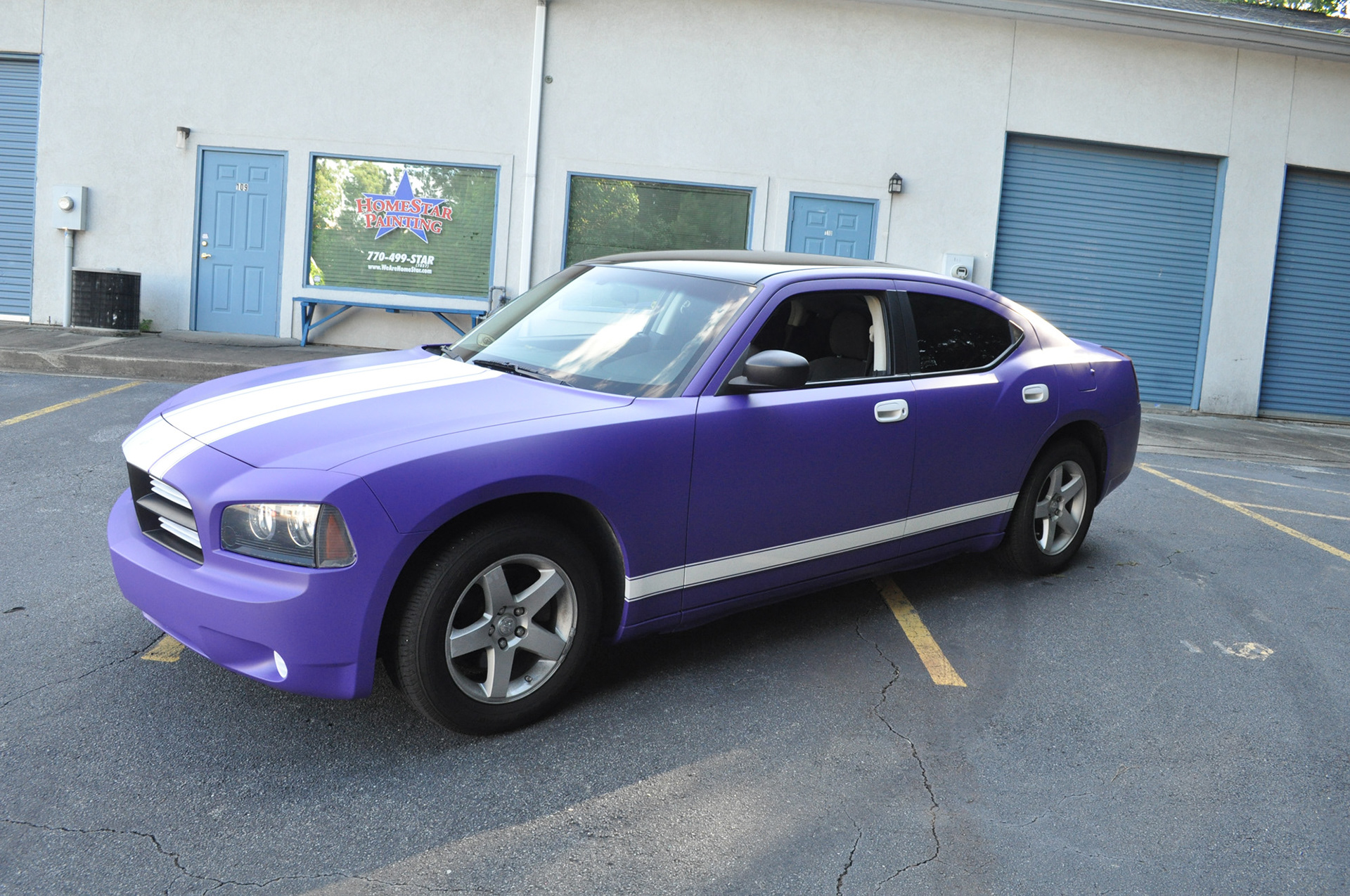 Purple Dodge Charger with white hood and lower-body stripes parked outside the workshop.